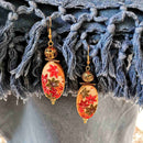 Σκουλαρίκια γυναικεία κρεμαστά με χρυσαφί χάντρα και οβάλ στολίδι με φύλλα σε πορτοκαλλί αποχρώσεις.