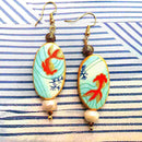 Σκουλαρίκια γυναικεία κρεμαστά και οβάλ στολίδι με πορτοκαλί ψάρι στον βυθό, και μαργαριταρένια χάντρα στο τελείωμα.